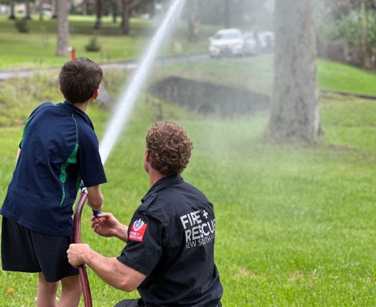 A student being shown how to use a fire hose by a fireman